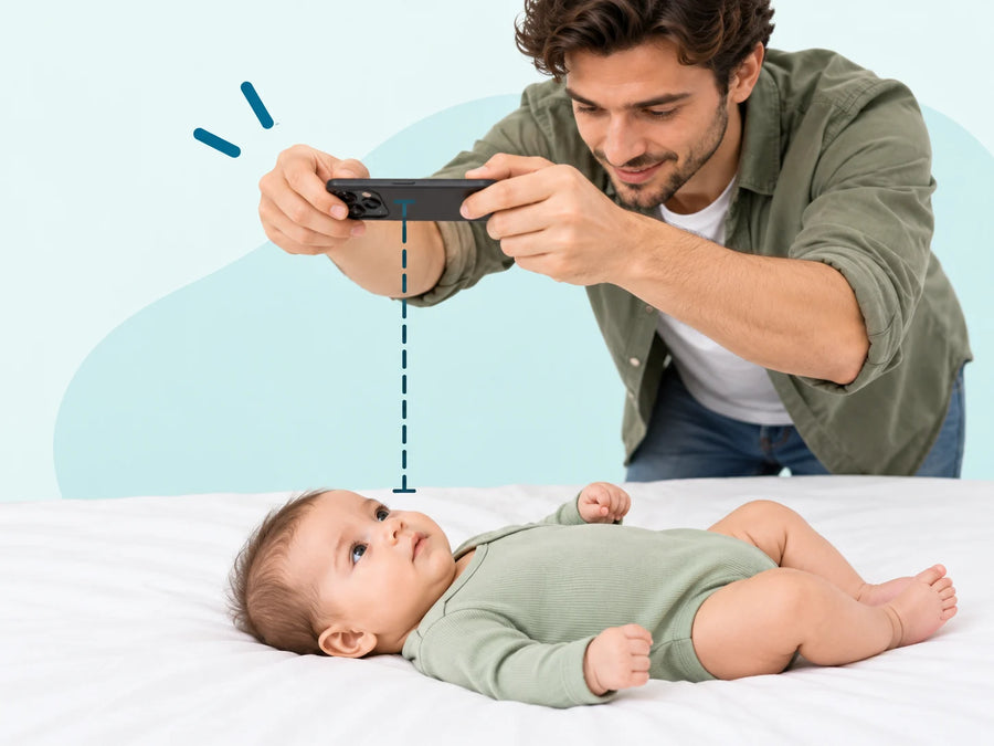 A baby lying on a white sheet while a parent holds a phone flat above her face